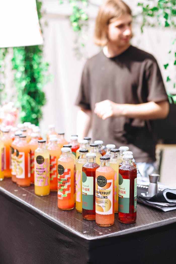Vibrant selection of assorted juice bottles at a market stall with vendor in background.